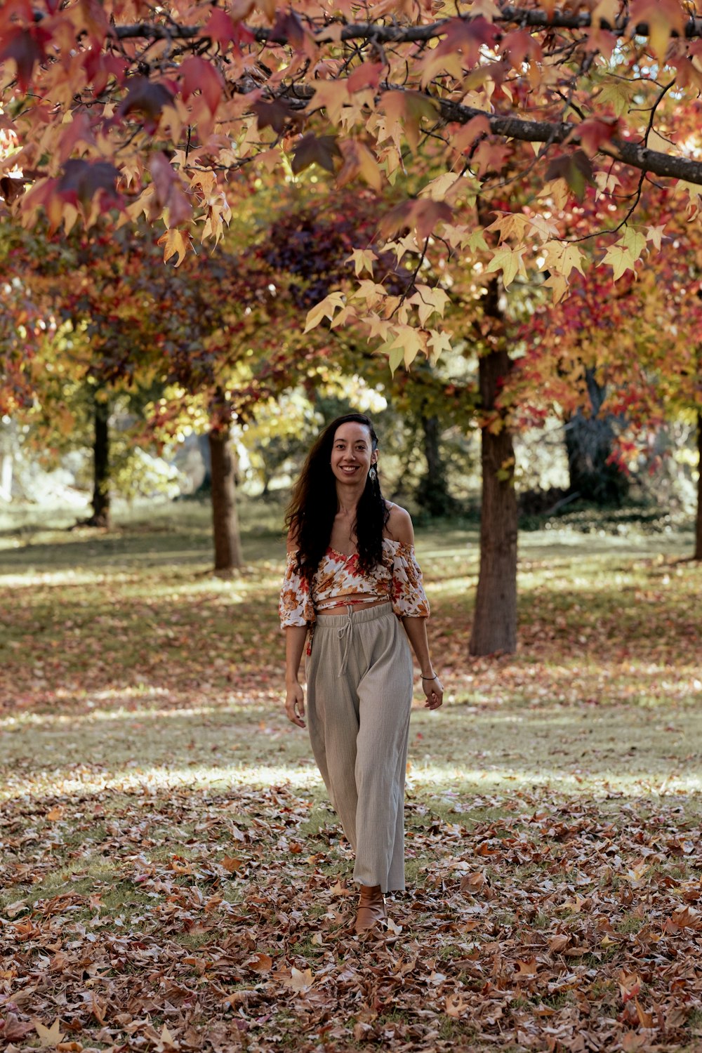 a woman walking through a leaf covered park
