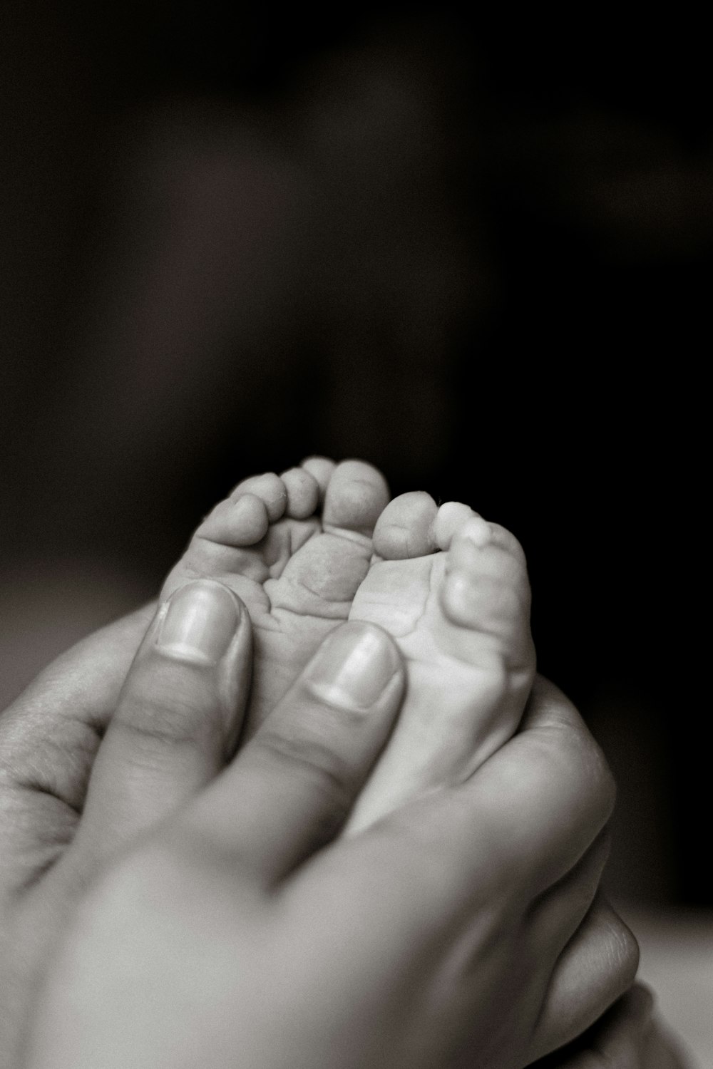 a black and white photo of a person holding a baby's foot