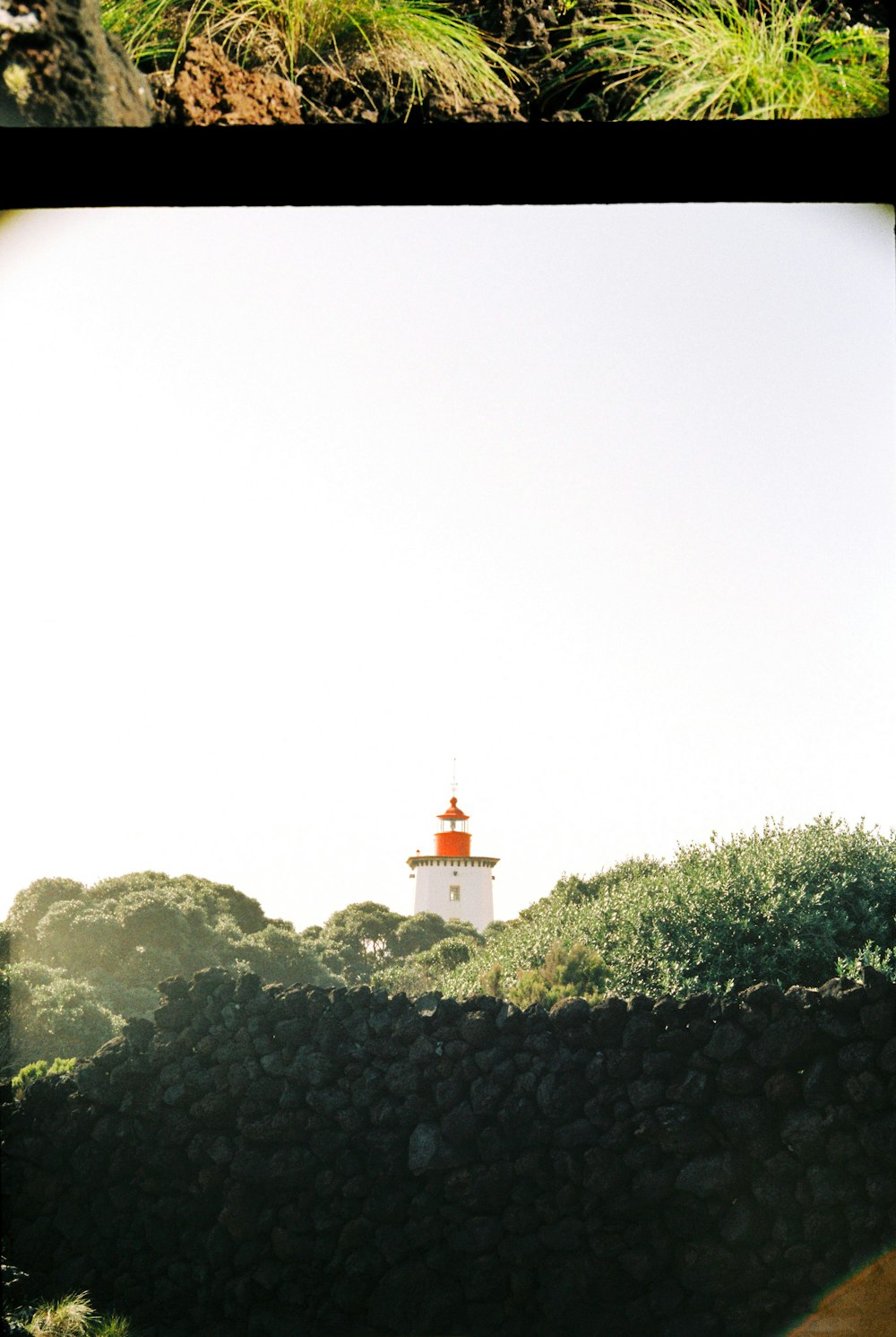 um farol vermelho e branco sentado no topo de uma colina