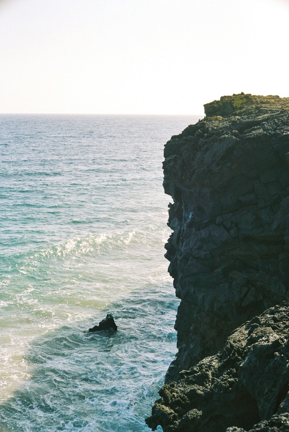 eine Person, die am Rande einer Klippe neben dem Meer steht