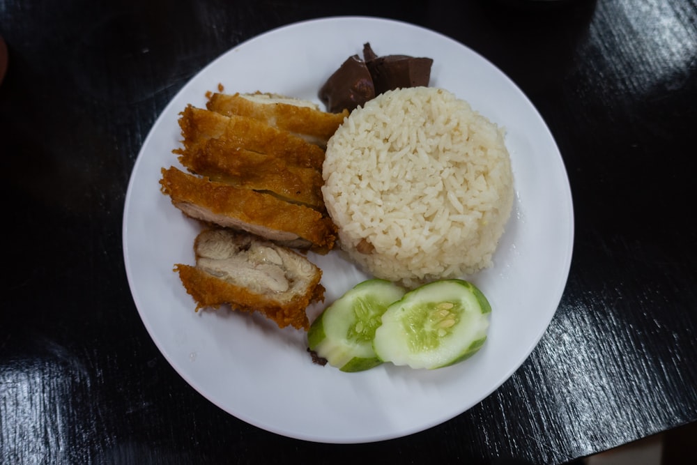a white plate topped with rice, meat and cucumbers