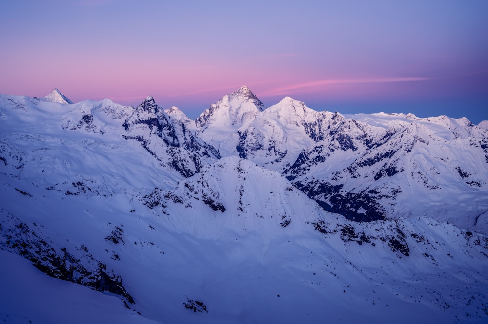 a snowy mountain range with a pink sky in the background