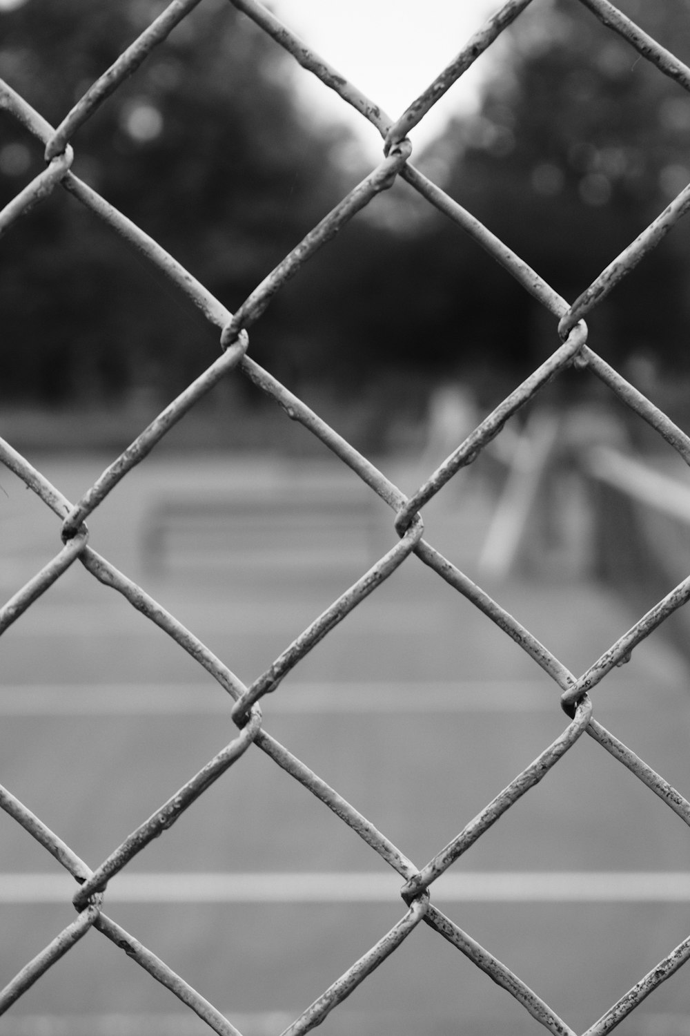 uma foto em preto e branco de uma quadra de tênis através de uma cerca de elo de corrente
