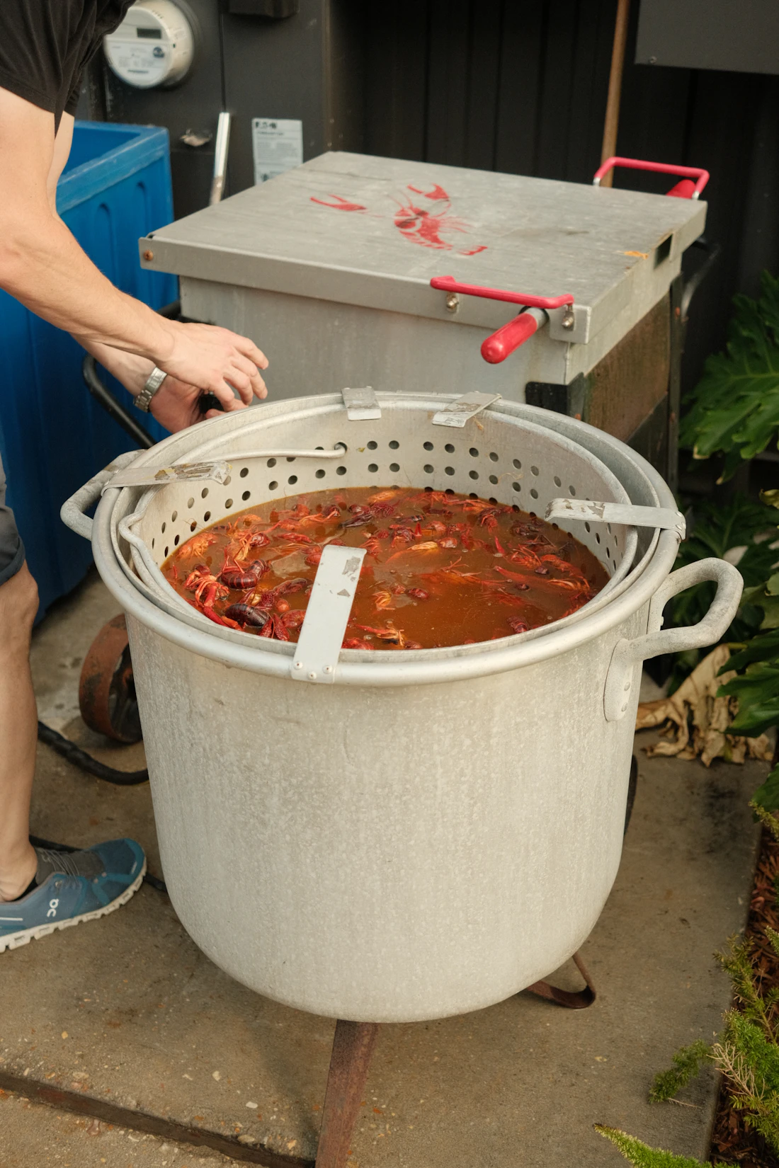 A tall aluminum pot full of crawfish in boil liquid, being tended outdoors