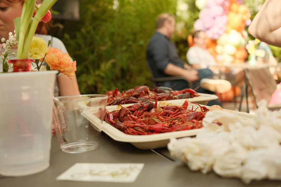 A long outdoor table set with a paper tray of boiled crawfish and guests seated around it