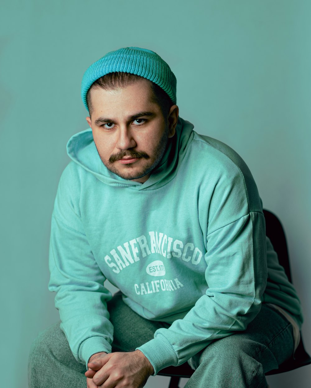 a man sitting on a chair wearing a green hoodie