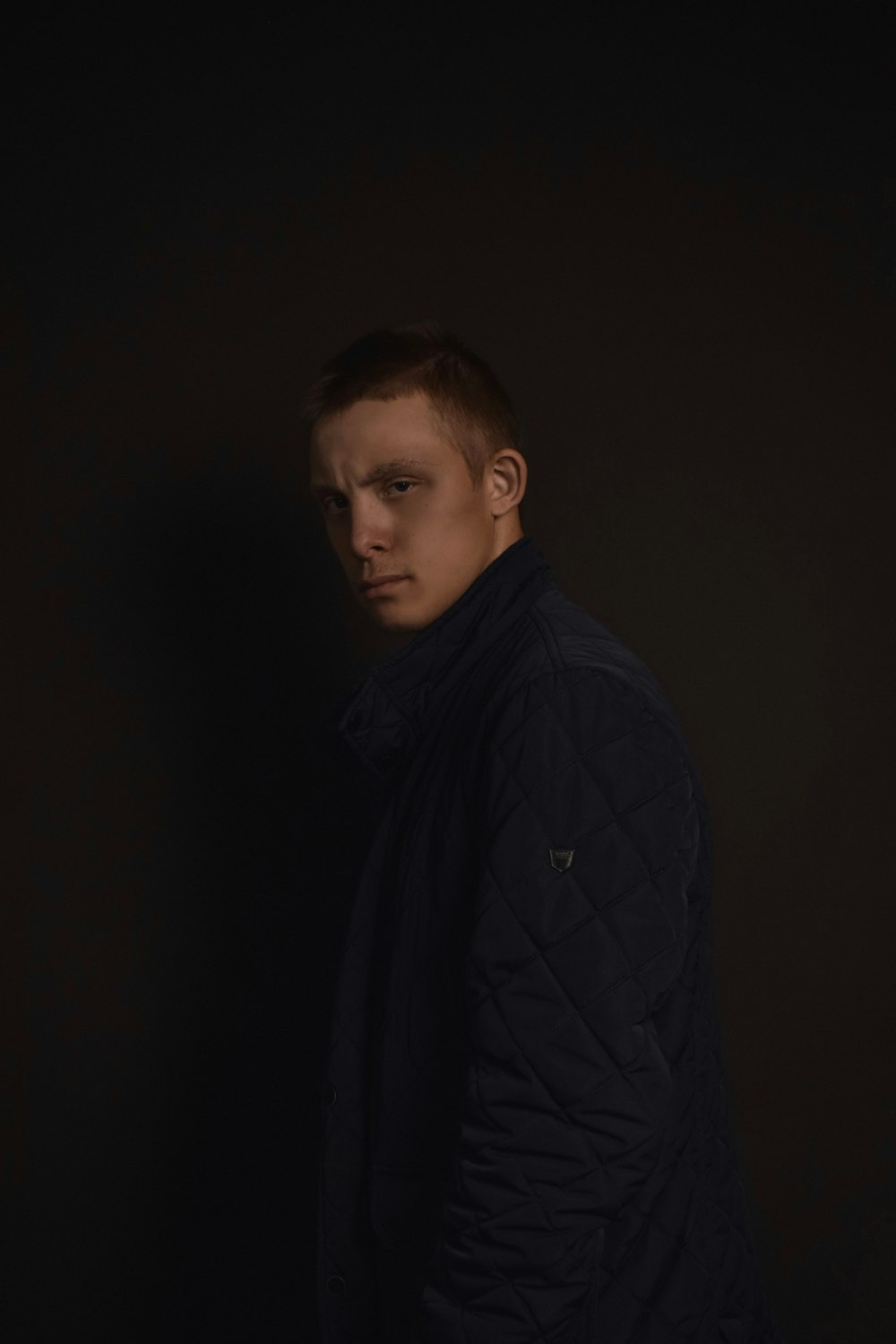 a man standing in a dark room wearing a black jacket