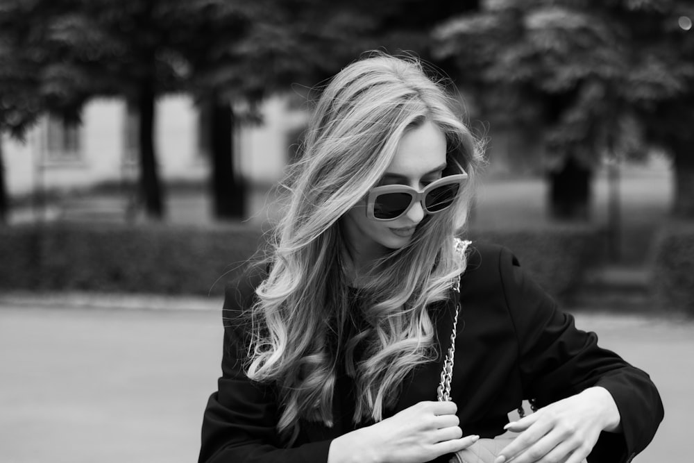 a woman in a black jacket and sunglasses looking at her cell phone