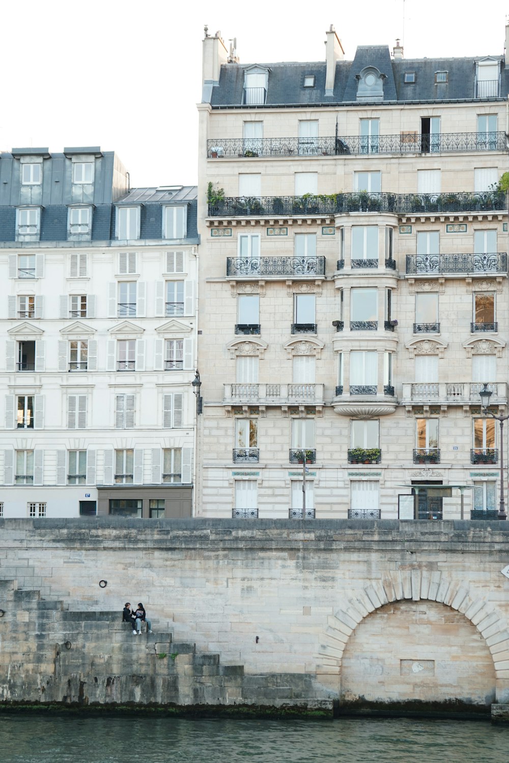 a couple of people sitting on a ledge next to a body of water