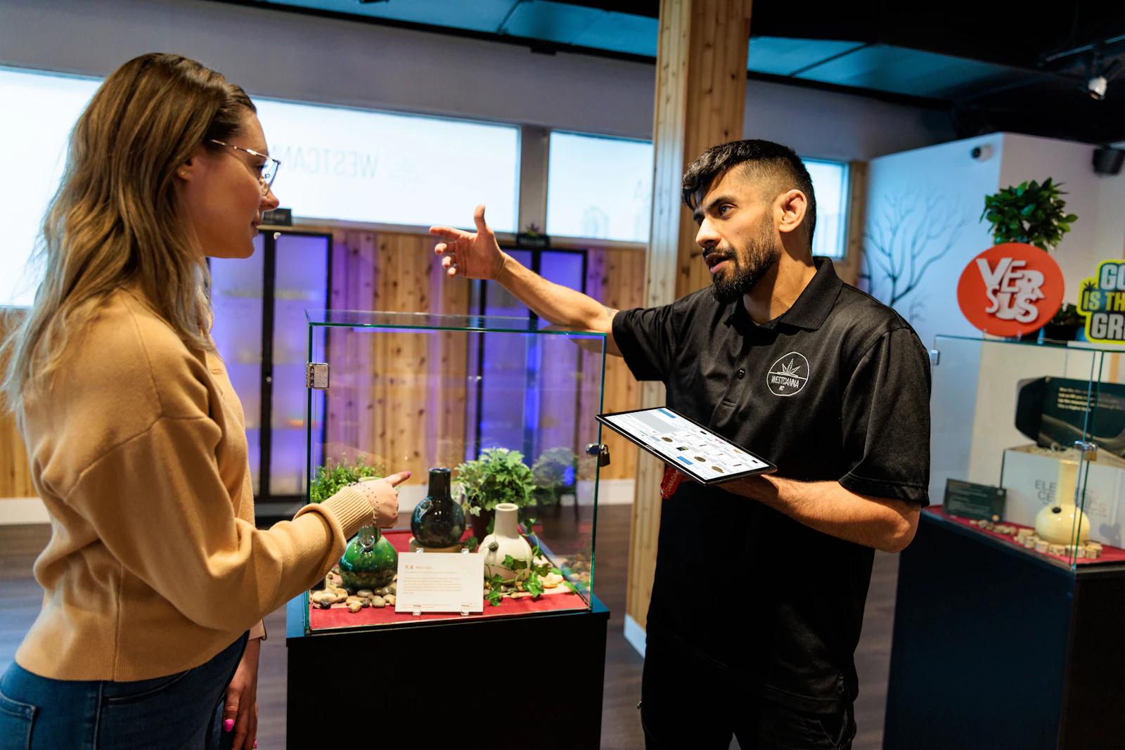 A budtender holding a tablet walks a customer through products on the dispensary floor, the personal service a customer profile makes possible