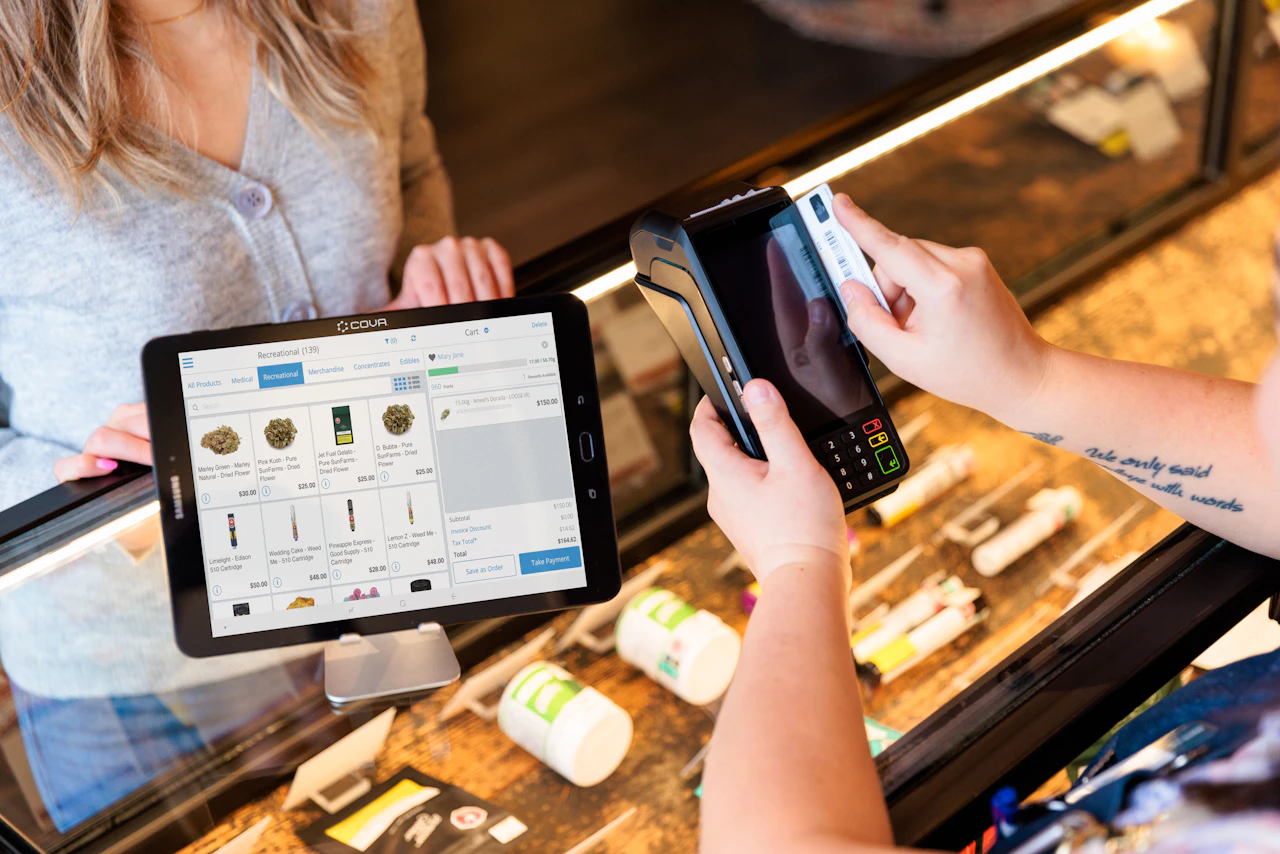 Dispensary staff member using a tablet to reconcile product counts against the display case during an inventory audit
