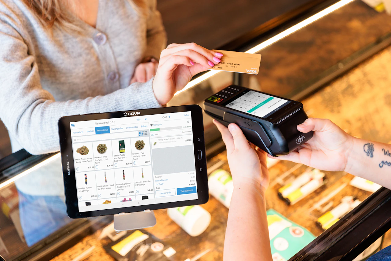 Customer paying by card at a dispensary counter using a compliant cannabis payment terminal connected to the POS