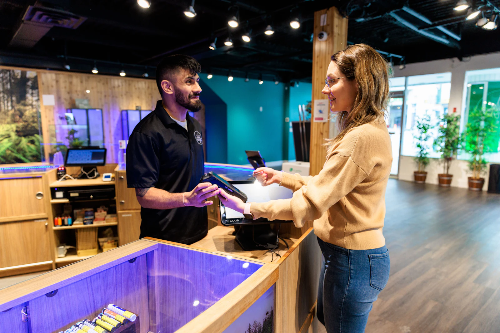 A budtender and customer at a dispensary checkout counter with a card terminal, where promotion rules apply to the sale automatically