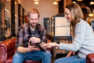a man and a woman sitting on a couch looking at a tablet