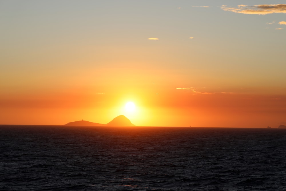 the sun setting over the ocean with a small island in the distance