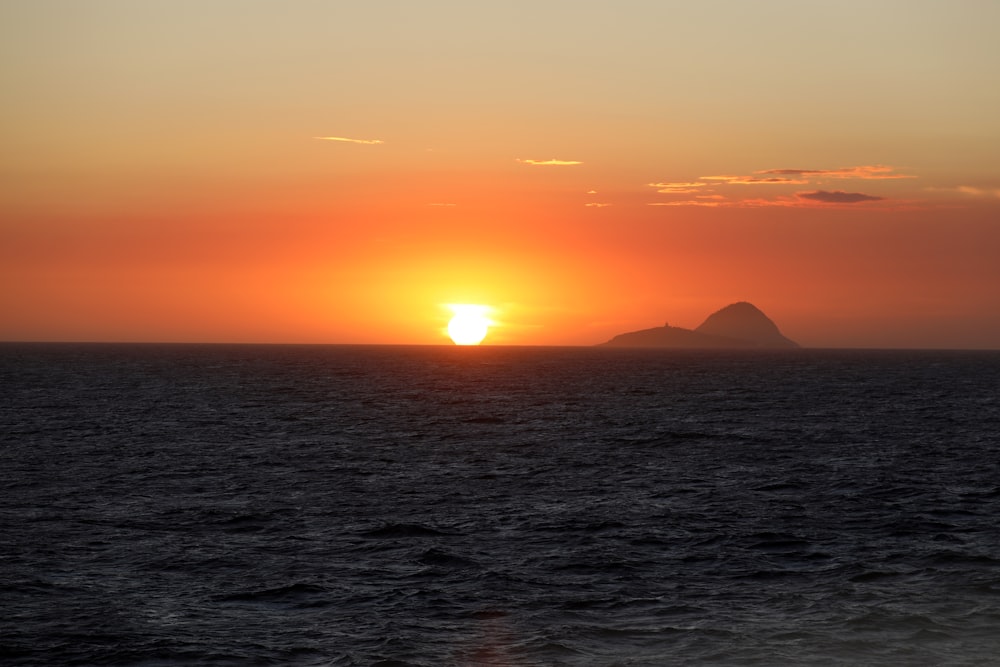 um pôr do sol sobre o oceano com uma pequena ilha ao longe