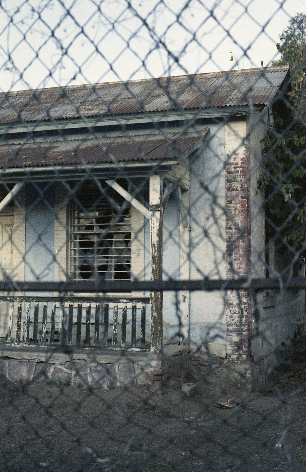 an old run down house behind a chain link fence