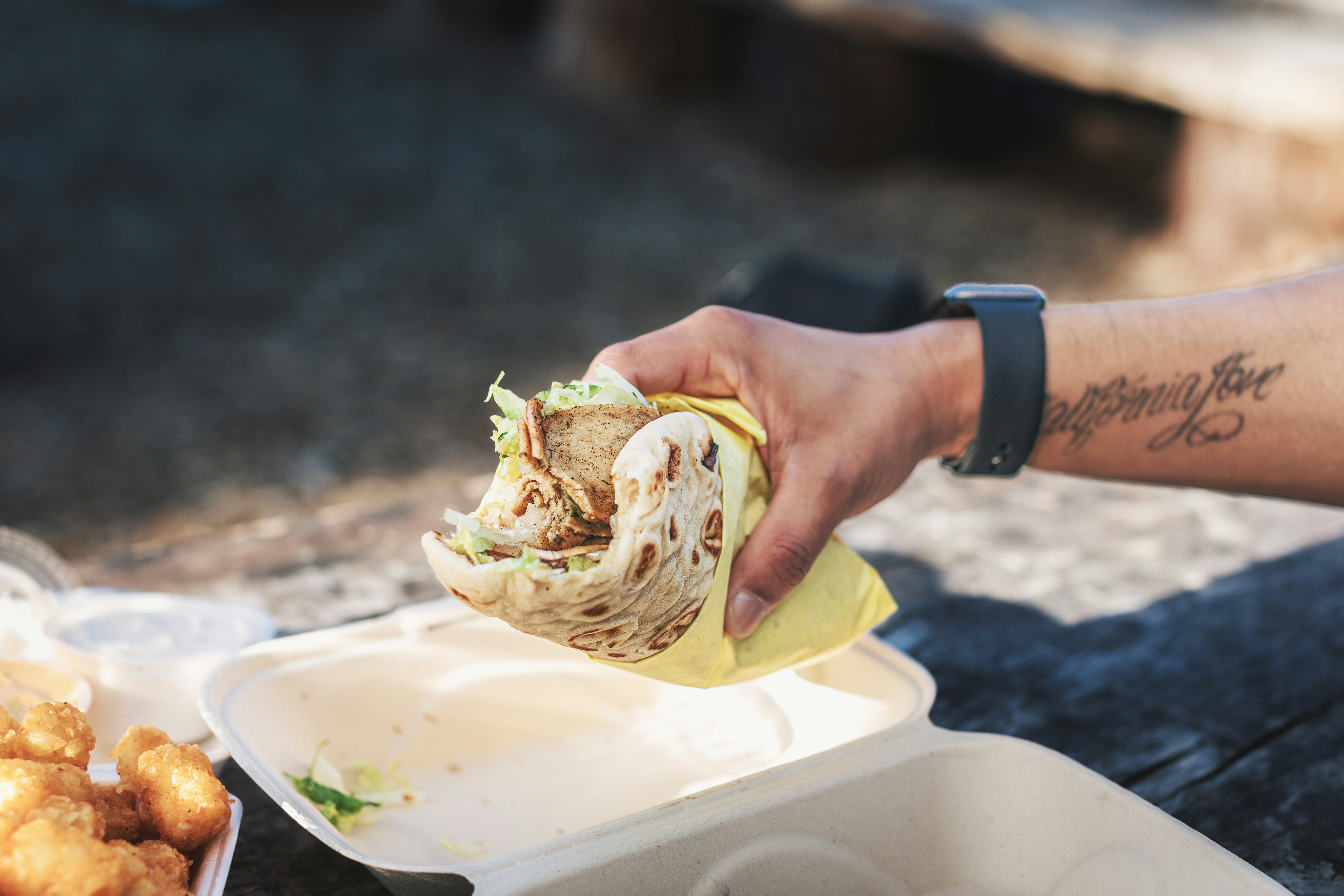 a person holding a burrito over a tray of food