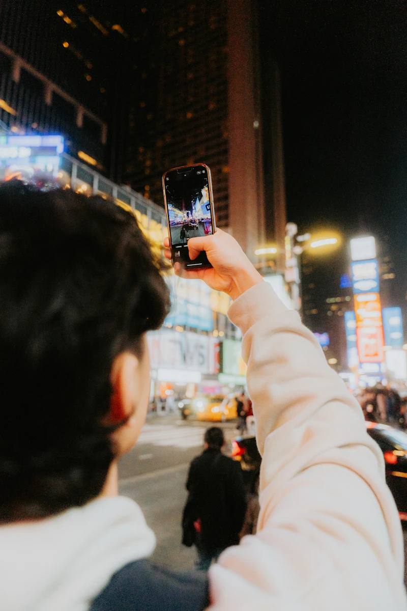 A traveller holding a phone in a lit-up city street at night