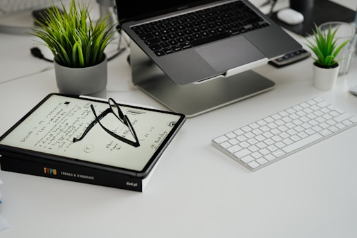 a desk with a laptop, keyboard, glasses and a potted plant