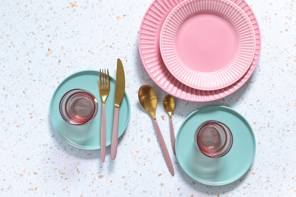 a pink and blue table setting with goldware