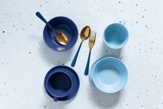a table topped with blue bowls and gold spoons