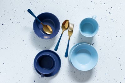 a table topped with blue bowls and gold spoons