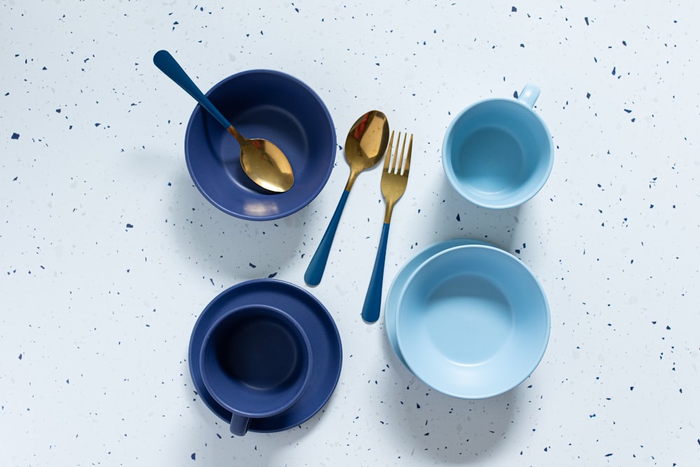 a table topped with blue bowls and gold spoons