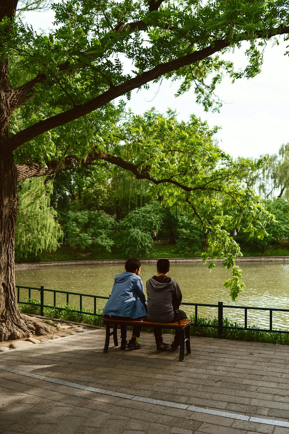 two people sitting on a bench next to a river
