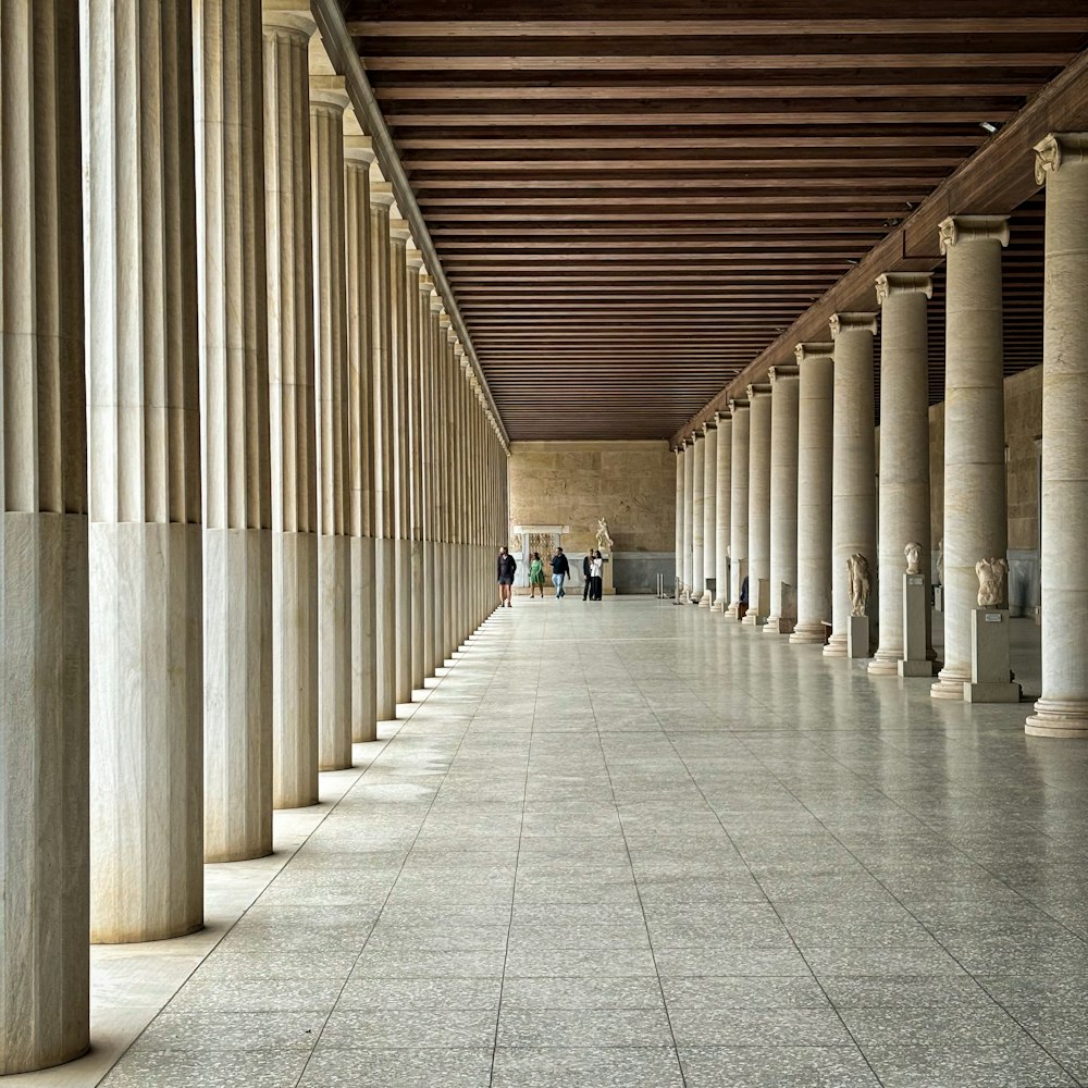 a long hallway with columns and people walking by