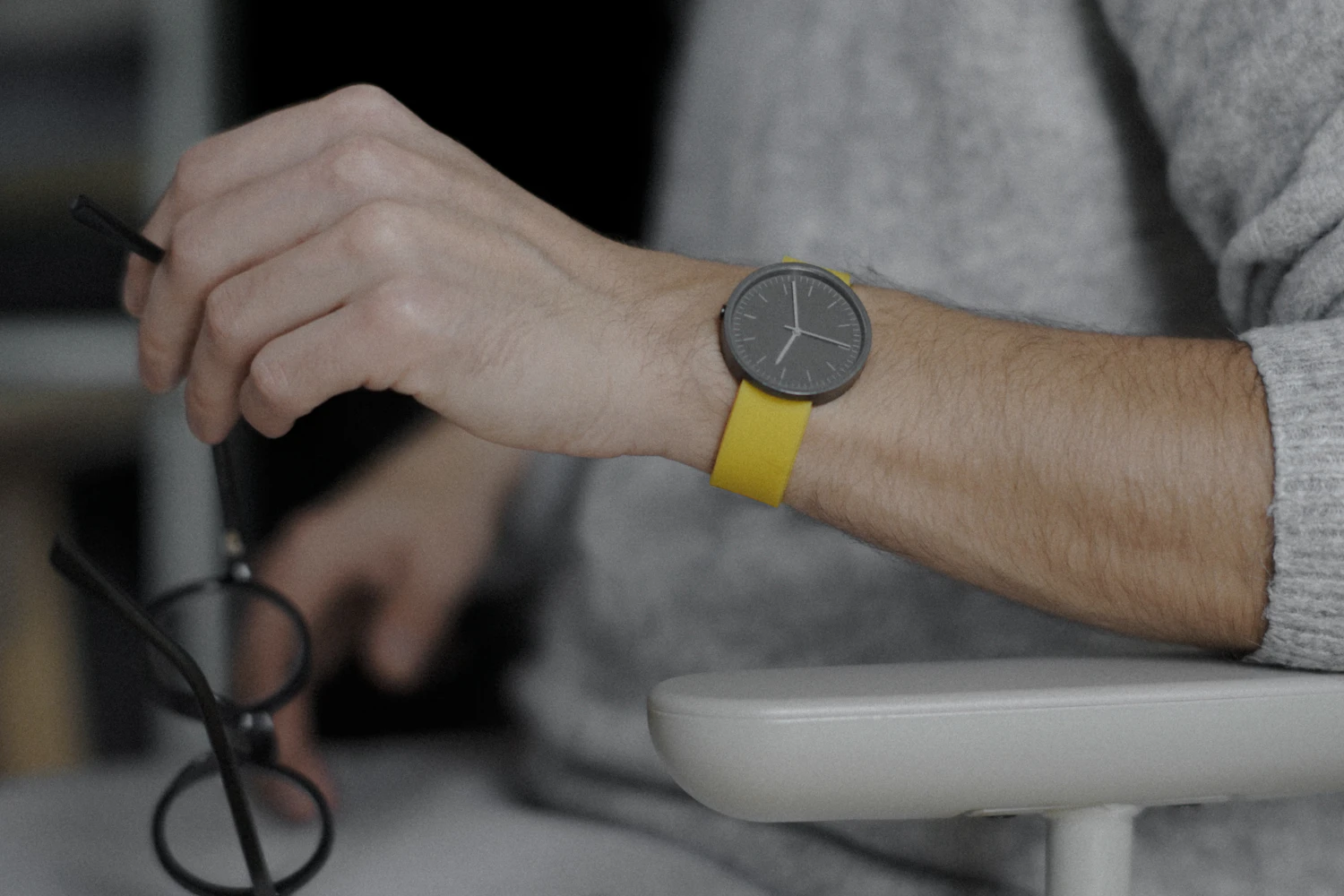 Jura 38 Slate, a slate-grey dial on a mustard rubber strap on a wrist holding a pair of glasses