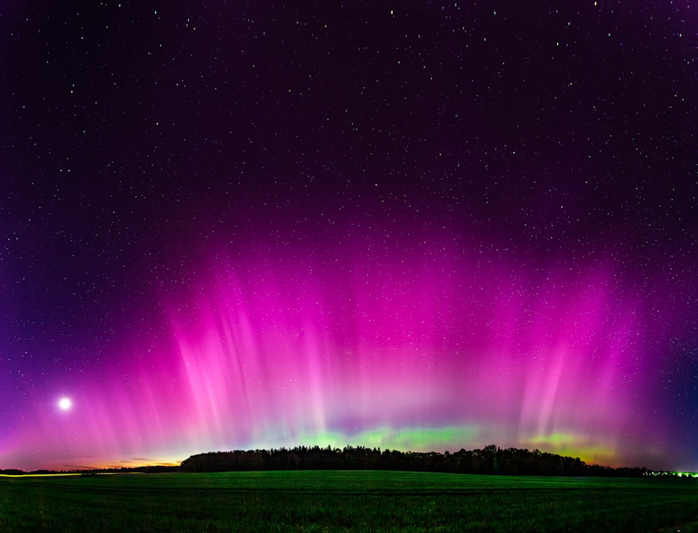 a bright purple and green aurora bore over a field