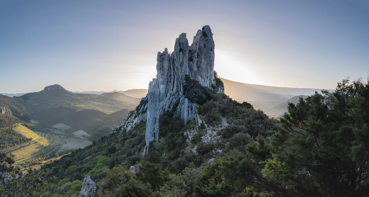 A limestone spire of the Dentelles de Montmirail in low sun, with wooded hills behind