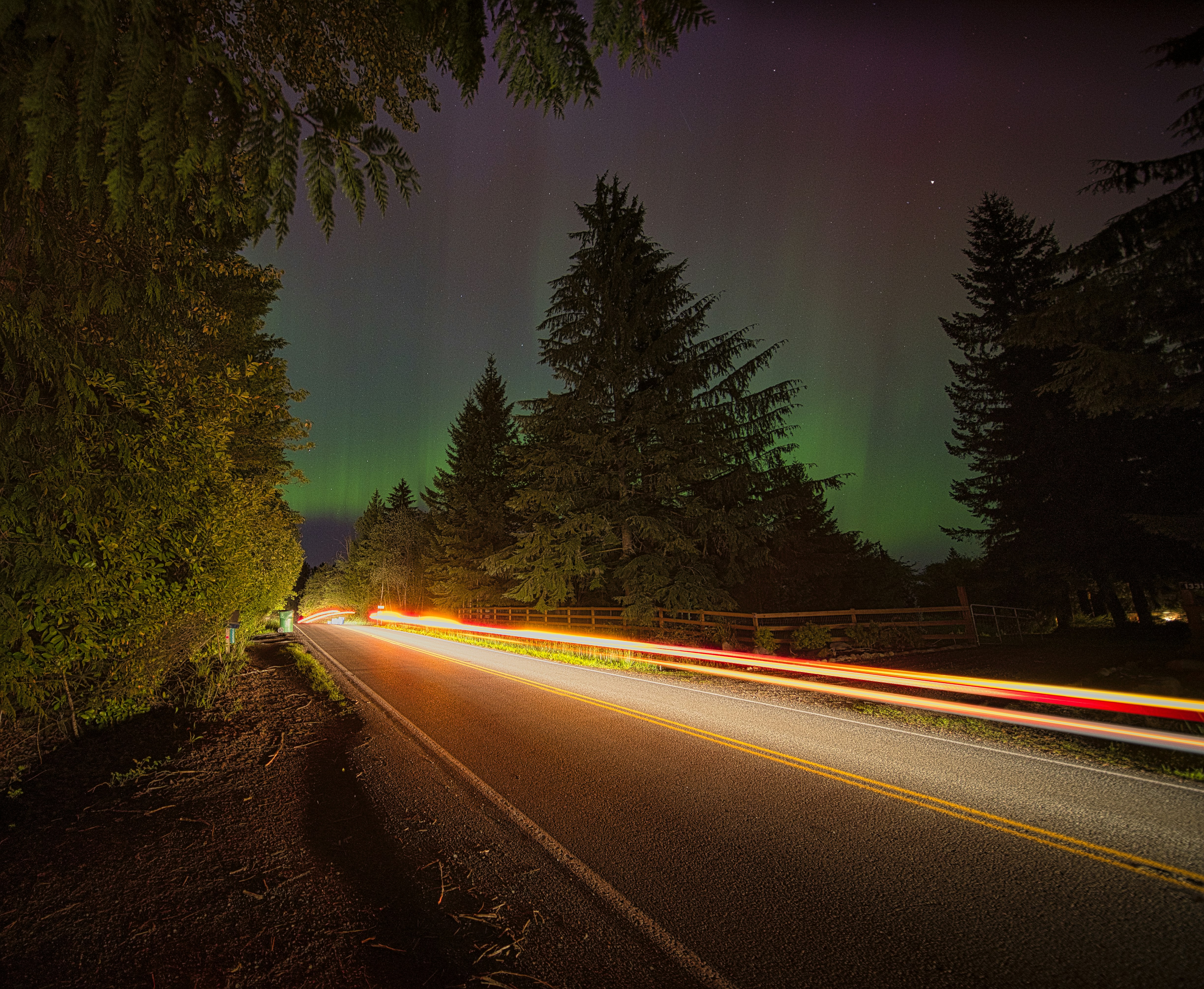 a long exposure photo of a road with the aurora lights in the background