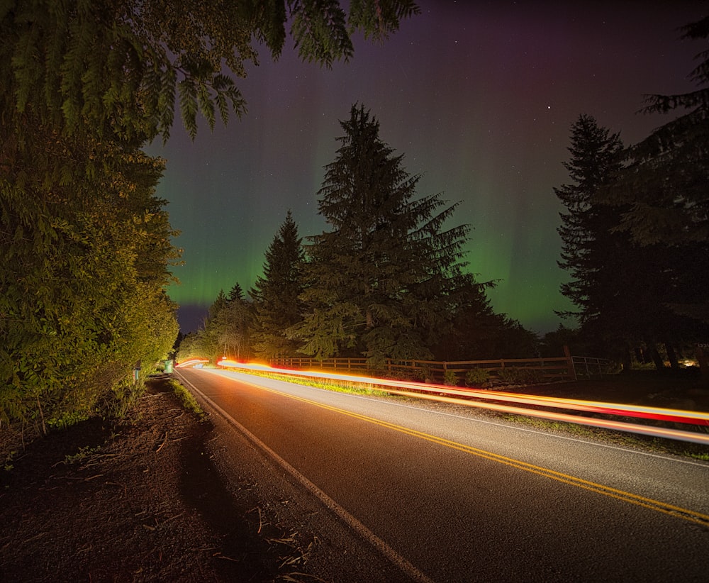 a long exposure photo of a road with the aurora lights in the background