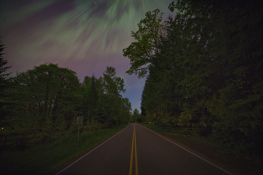 a long road with a green and purple aurora bore in the sky