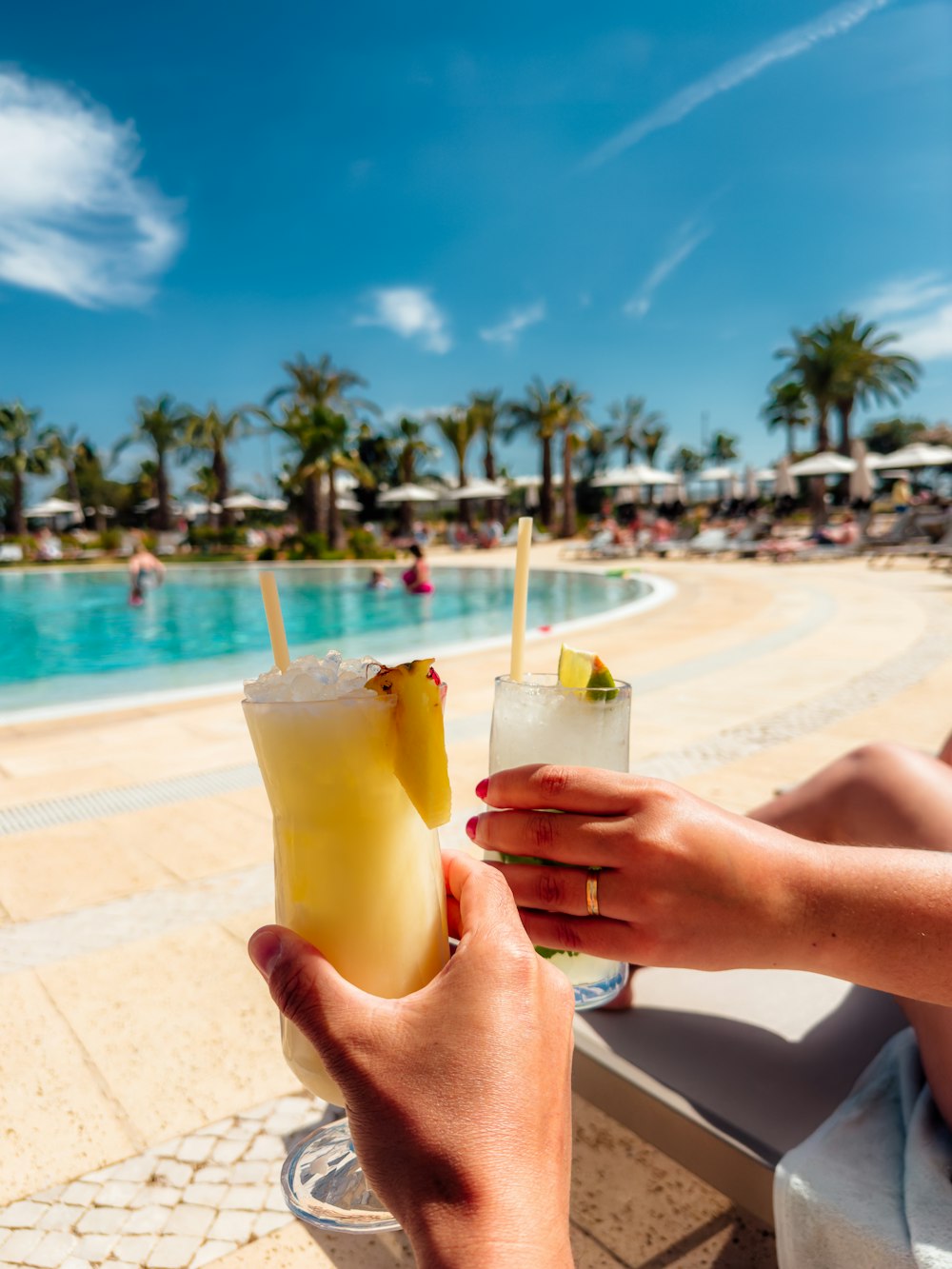 a person holding a drink in front of a swimming pool