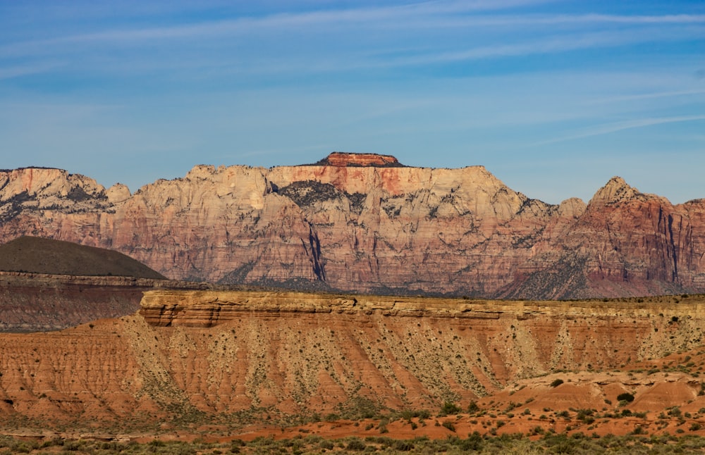 a mountain range with a red rock formation in the foreground