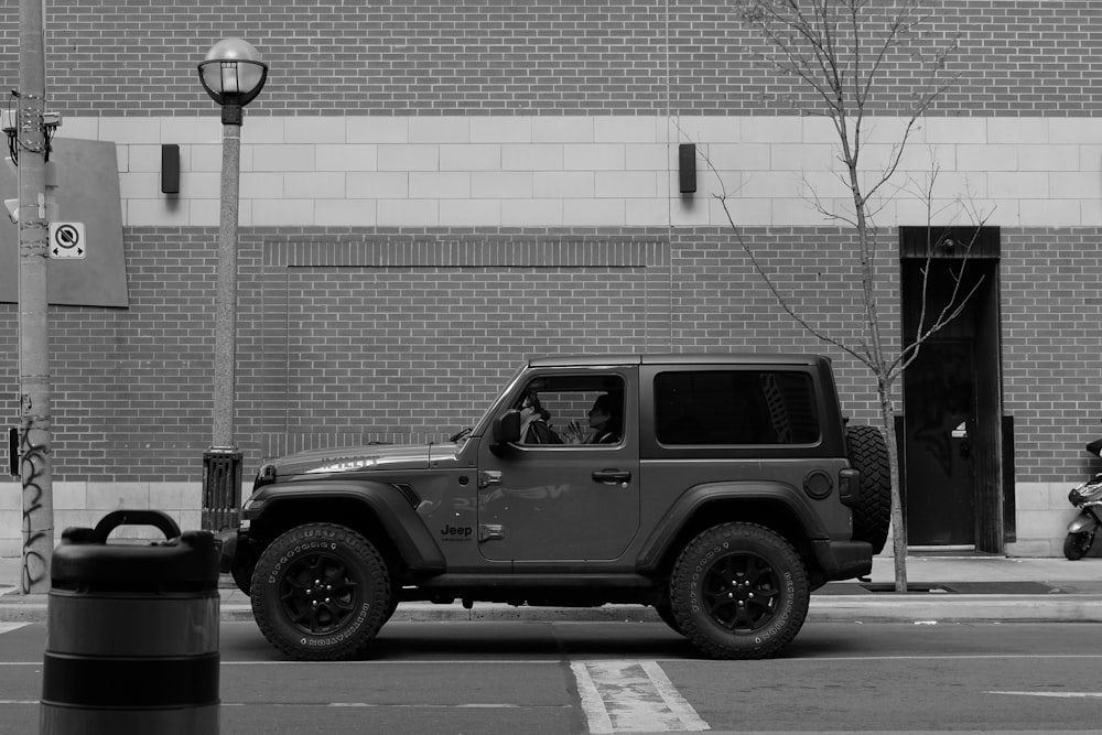 a black and white photo of a jeep parked in front of a building