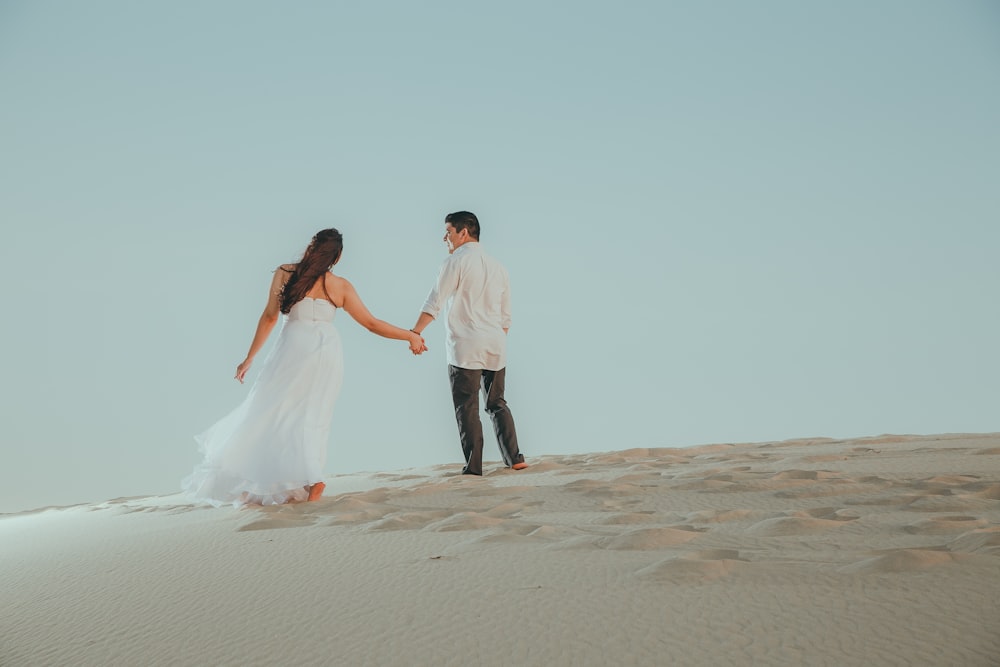 a man and a woman holding hands and walking in the sand