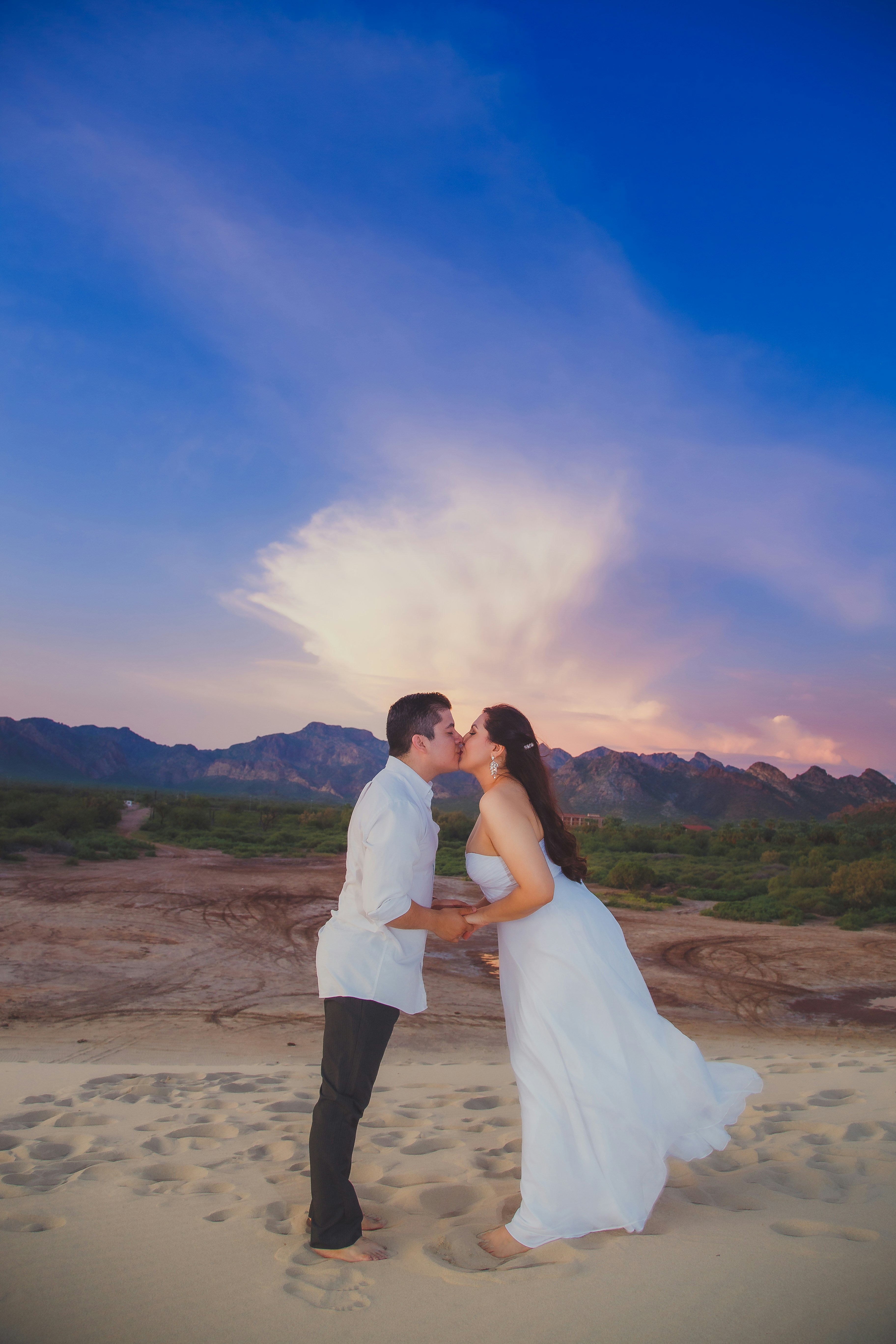 a bride and groom kissing on the beach