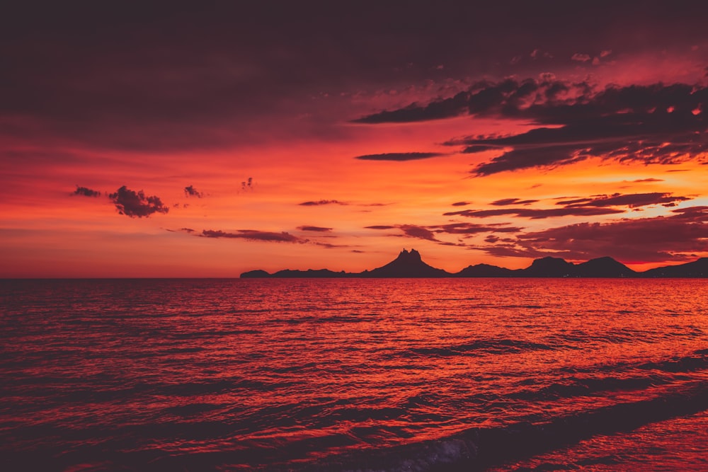 a red sunset over the ocean with mountains in the distance