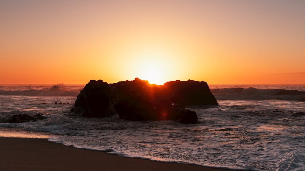 the sun is setting over the ocean with rocks in the foreground