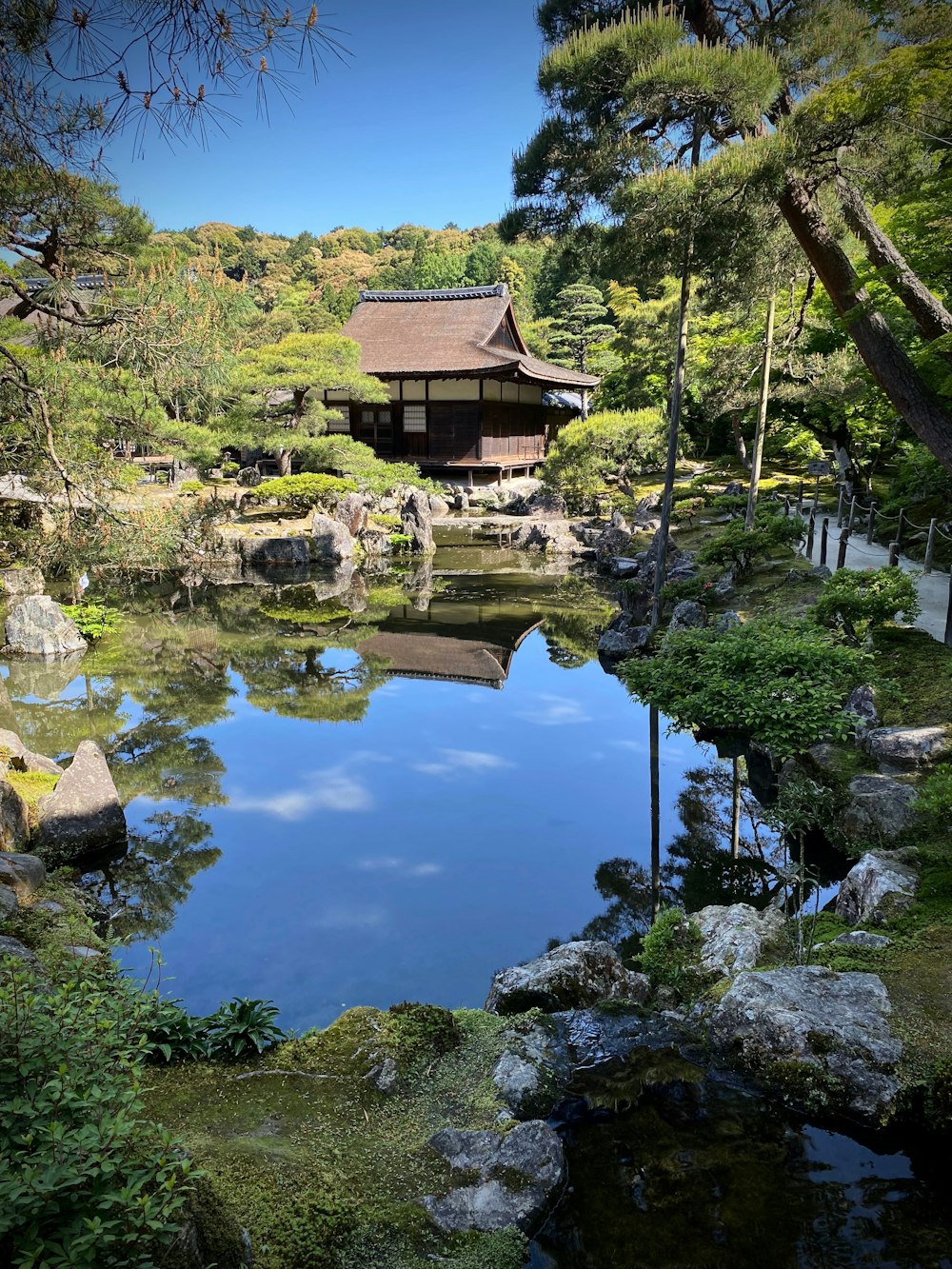 a pond surrounded by rocks and trees with a building in the background