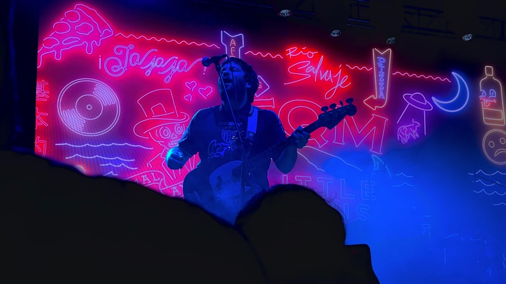 a man playing a guitar in front of a neon sign