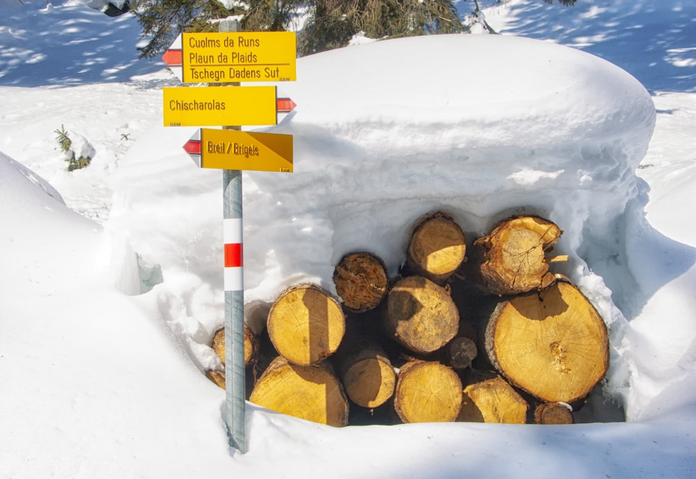 a pile of logs sitting in the snow next to a sign