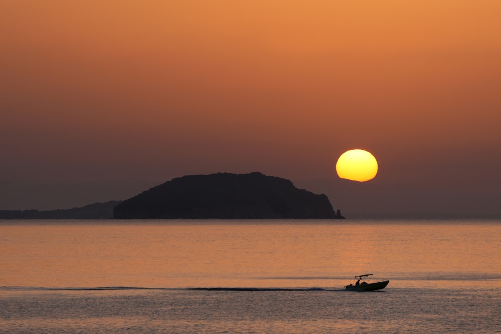 a boat in the water at sunset with a small island in the background