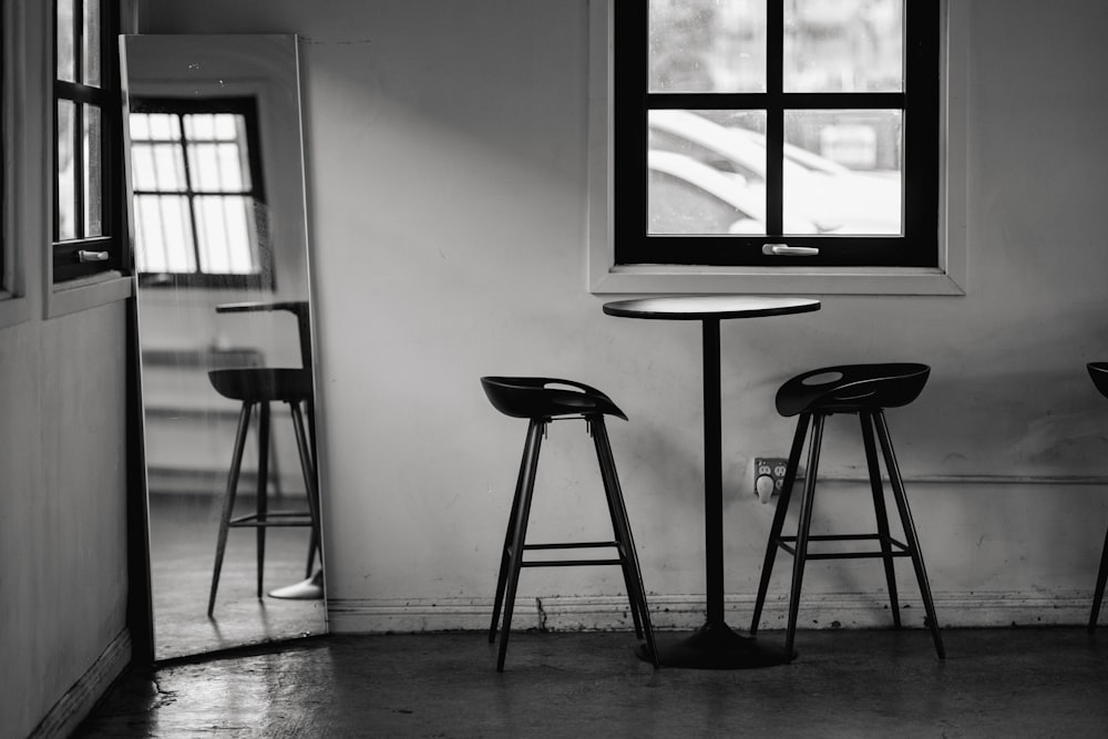 a black and white photo of three stools and a table