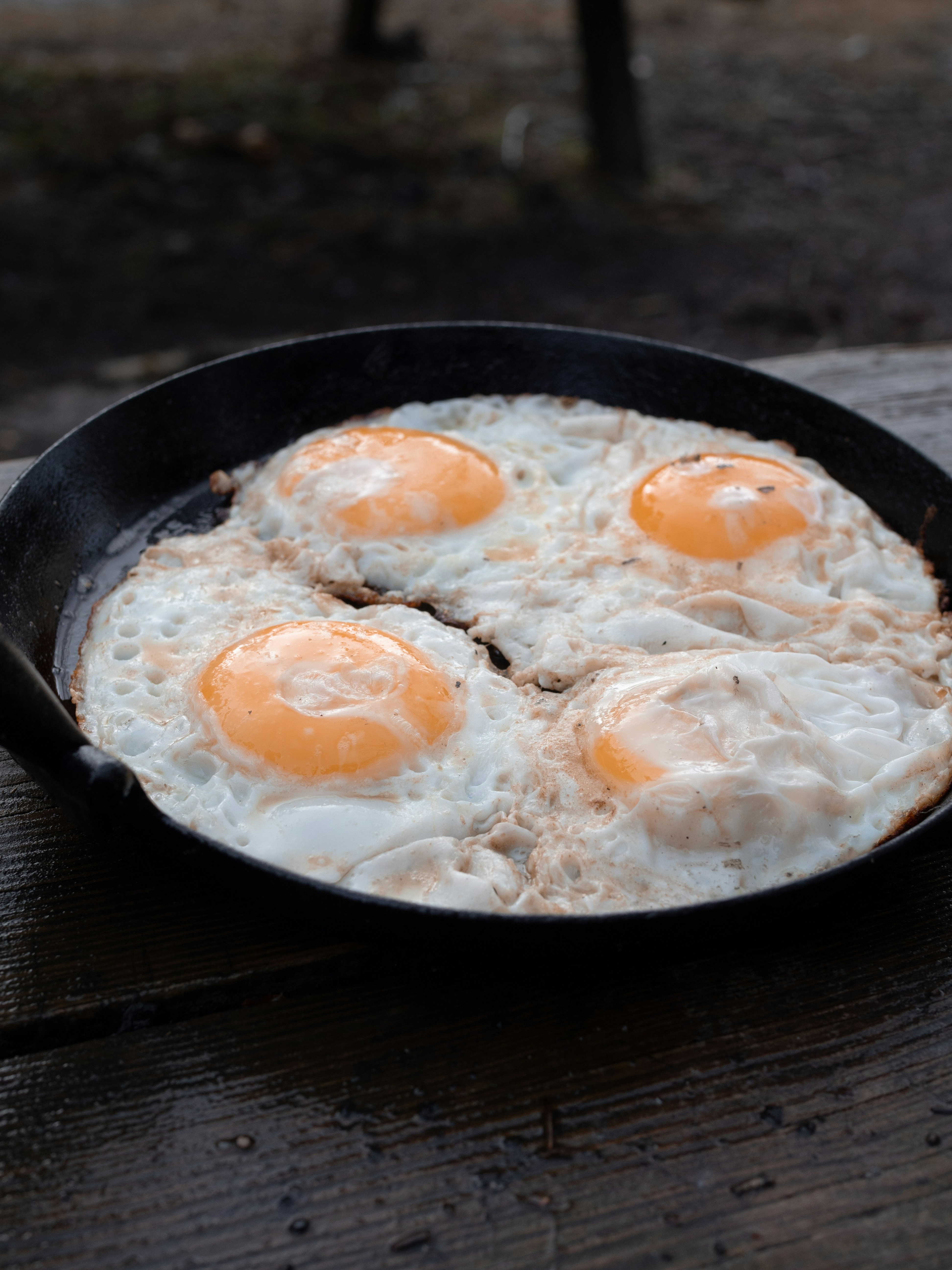 three fried eggs in a skillet on a picnic table