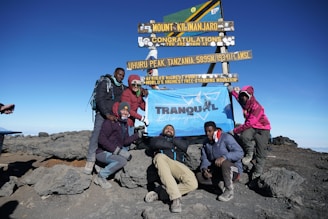 a group of people standing next to a sign on top of a mountain